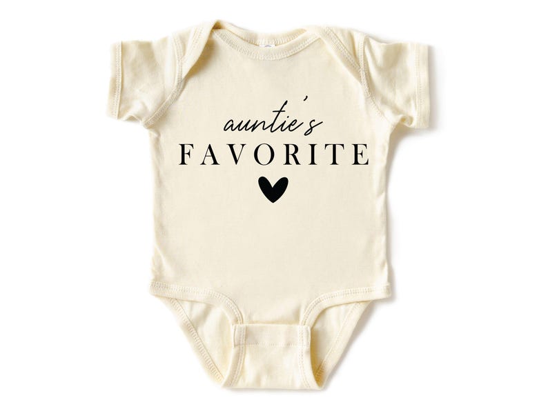 May include: A cream-coloured baby onesie with short sleeves and a black graphic that reads "auntie's FAVORITE" with a small black heart.