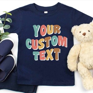 May include: A navy blue t-shirt with the text "YOUR CUSTOM TEXT" in colorful, outlined letters. The letters are in shades of teal, orange, pink, and brown.