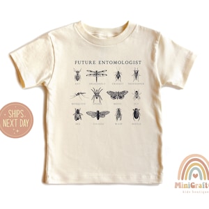 May include: A beige short-sleeved t-shirt with the text "FUTURE ENTOMOLOGIST" printed on the front. The shirt features illustrations of various insects, including an ant, dragonfly, cricket, treehopper, mosquito, spider, moth, fly, bee, cicada, wasp, and beetle.