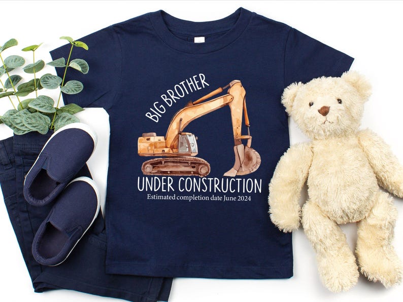 Pode incluir: Camiseta azul marinho para crian&ccedil;as com uma ilustra&ccedil;&atilde;o em aquarela de uma escavadeira de constru&ccedil;&atilde;o. A camisa diz "Irm&atilde;o Mais Velho em Constru&ccedil;&atilde;o" com uma data de conclus&atilde;o estimada em junho de 2024. Inclui sapatos, cal&ccedil;as e um ursinho de pel&uacute;cia azul marinho.