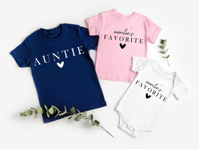 May include: Three t-shirts in different colours and designs. A navy blue t-shirt with the word "AUNTIE" in white text and a white heart. A pink t-shirt with the text "auntie's FAVORITE" in black text and a black heart. A white t-shirt with the text "auntie's FAVORITE" in black text and a black heart.