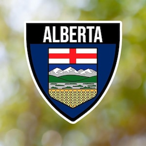 Può includere: Un adesivo a forma di scudo blu e bianco con la parola "ALBERTA" in lettere bianche in alto. Lo scudo presenta una croce bianca su sfondo rosso, montagne, un fiume e spighe di grano.