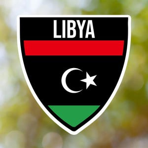 Pode incluir: Um adesivo preto, vermelho e verde em forma de escudo com a palavra "LIBYA" em letras brancas e uma lua crescente e uma estrela brancas.