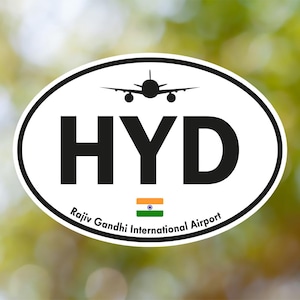 May include: Oval sticker with a white background and a black border. The sticker features the letters "HYD" in bold black font, a silhouette of an airplane, and the text "Rajiv Gandhi International Airport". An Indian flag is also present.