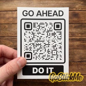 Pode incluir: Um autocolante retangular branco com o texto preto GO AHEAD no topo e DO IT na parte inferior. Centrado entre o texto está um código QR quadrado a preto e branco com uma margem preta espessa, concebido para digitalização e interação.
