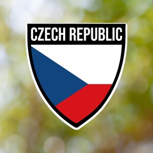 Può includere: Uno scudo bianco con un triangolo blu e un rettangolo rosso, che rappresenta la bandiera della Repubblica Ceca. Lo scudo è bordato di nero e ha il testo "CZECH REPUBLIC" in lettere bianche nella parte superiore.