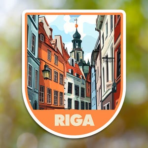 May include: A colorful illustration of a street scene in Riga, Latvia. The image features a narrow street lined with colorful buildings, a tall church spire, and a street lamp. The text "RIGA" is printed in bold letters at the bottom of the image.