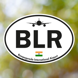 May include: Oval sticker with a black airplane silhouette above the letters "BLR" in bold black font. Below, the text "Kempegowda International Airport" is curved along the bottom, with the Indian flag in the center.