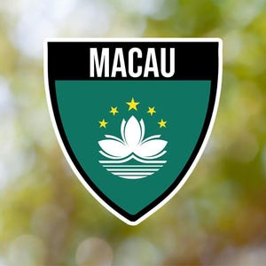 Może przedstawiać: Zielona i czarna naklejka w kształcie tarczy z napisem "MACAU" białymi literami u góry. W środku naklejki znajduje się biały kwiat lotosu z pięcioma żółtymi gwiazdami wokół, wszystko na zielonym tle.