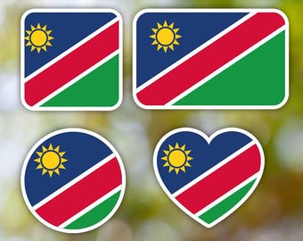 Könnte beinhalten: Vier Aufkleber in verschiedenen Formen mit der Flagge Namibias. Die Flagge ist blau mit einem roten diagonalen Streifen und einem grünen Streifen. Eine gelbe Sonne mit 12 Strahlen befindet sich in der oberen linken Ecke der Flagge.