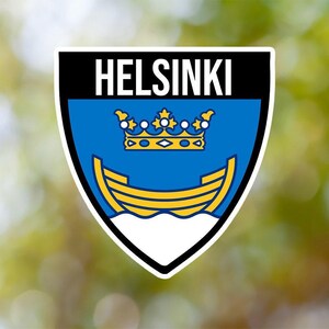 May include: A blue and white shield-shaped emblem with the word "HELSINKI" in black text at the top. The shield features a gold crown and a yellow boat on a blue wave.
