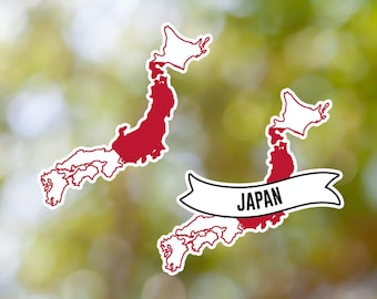 May include: Two stickers featuring the map of Japan. The main island is filled with red, with white outlines. One sticker has a banner with the word "JAPAN". The background is a blurred green and yellow.