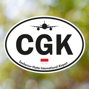 Pode incluir: Adesivo oval com fundo branco e borda preta. Apresenta as letras "CGK" em negrito preto, uma silhueta de avião e o texto "Soekarno-Hatta International Airport". Uma pequena bandeira indonésia também está presente.
