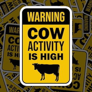 Op de afbeelding: Een geel waarschuwingsbord met zwarte tekst die "WAARSCHUWING KOE ACTIVITEIT IS HOOG" luidt. Een zwart silhouet van een koe bevindt zich in het midden van het bord.