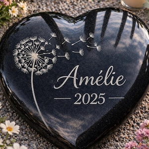 Peut inclure: Une pierre tombale noire en forme de cœur, gravée du nom "Amélie" et de l'année "2025", ainsi qu'un motif de pissenlit. La pierre est entourée de fleurs et d'une bougie allumée, créant une scène sereine.