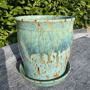 以下が含まれることがあります： ターコイズ色のセラミック植木鉢と、お揃いの受け皿。 植木鉢は、茶色と白のアクセントと、滴る釉薬効果のある光沢仕上げです。 植木鉢は円筒形で、わずかにフレアしたリムが付いています。