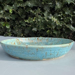 以下が含まれることがあります： ターコイズ色の釉薬と茶色の斑点のある、大きな楕円形のセラミック製のサービングボウル。ボウルはわずかに盛り上がった縁を持っています。