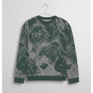 K&ouml;nnte beinhalten: Ein gr&uuml;nes und graues Sweatshirt mit einem Quallenmuster. Der Rundhalsausschnitt und die B&uuml;ndchen sind einfarbig dunkelgr&uuml;n. Das Quallendesign ist hellgr&uuml;n und grau und erzeugt einen strukturierten Unterwasser-Effekt. Das Sweatshirt h&auml;ngt an einem wei&szlig;en Kleiderb&uuml;gel.