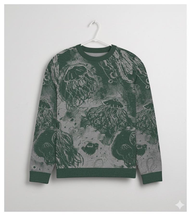 K&ouml;nnte beinhalten: Ein gr&uuml;nes und graues Sweatshirt mit einem Quallenmuster. Der Rundhalsausschnitt und die B&uuml;ndchen sind einfarbig dunkelgr&uuml;n. Das Quallendesign ist hellgr&uuml;n und grau und erzeugt einen strukturierten Unterwasser-Effekt. Das Sweatshirt h&auml;ngt an einem wei&szlig;en Kleiderb&uuml;gel.