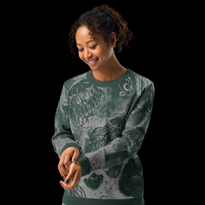 K&ouml;nnte beinhalten: Ein dunkelgr&uuml;ner Pullover mit einem grauen, abstrakten Design. Der Pullover hat einen Rundhalsausschnitt und lange &Auml;rmel mit gerippten B&uuml;ndchen. Das Design ist eine Mischung aus organischen Formen und Mustern, die einen einzigartigen, k&uuml;nstlerischen Look erzeugen.