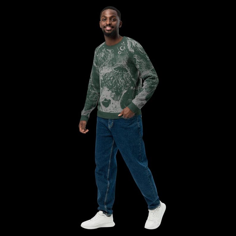 K&ouml;nnte beinhalten: Ein gr&uuml;n-grau gemustertes Sweatshirt. Das Sweatshirt hat ein einzigartiges Design mit einer Mischung aus Gr&uuml;n- und Graut&ouml;nen. Die Person tr&auml;gt eine blaue Jeans und wei&szlig;e Turnschuhe. Der Hintergrund ist schwarz.