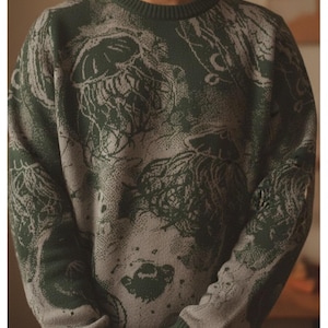 K&ouml;nnte beinhalten: Gr&uuml;ner und grauer Rundhals-Pullover mit einem einzigartigen Muster. Der Pullover hat eine dunkelgr&uuml;ne Grundfarbe mit einem hellgrauen, abstrakten Design. Die B&uuml;ndchen und der Halsausschnitt sind einfarbig dunkelgr&uuml;n. Der Pullover ist aus weichem Strickmaterial.