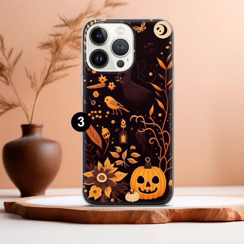 May include: A clear phone case with a black and orange design. The design features a bird, a pumpkin, and a variety of floral elements. The case is compatible with iPhone models.
