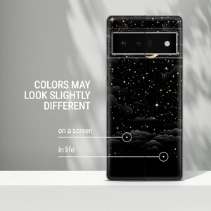 Puede incluir: Una funda de tel&eacute;fono negra con un dise&ntilde;o de noche estrellada con estrellas doradas, una luna creciente y nubes. La funda tiene un recorte para el objetivo de la c&aacute;mara.