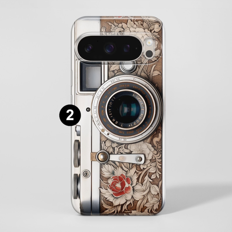 Pu&ograve; includere: Una custodia per telefono con un design di fotocamera vintage. La custodia ha una combinazione di colori argento e marrone con accenti floreali e una rosa rossa. L'obiettivo della fotocamera &egrave; dettagliato con testo e una lente nera.