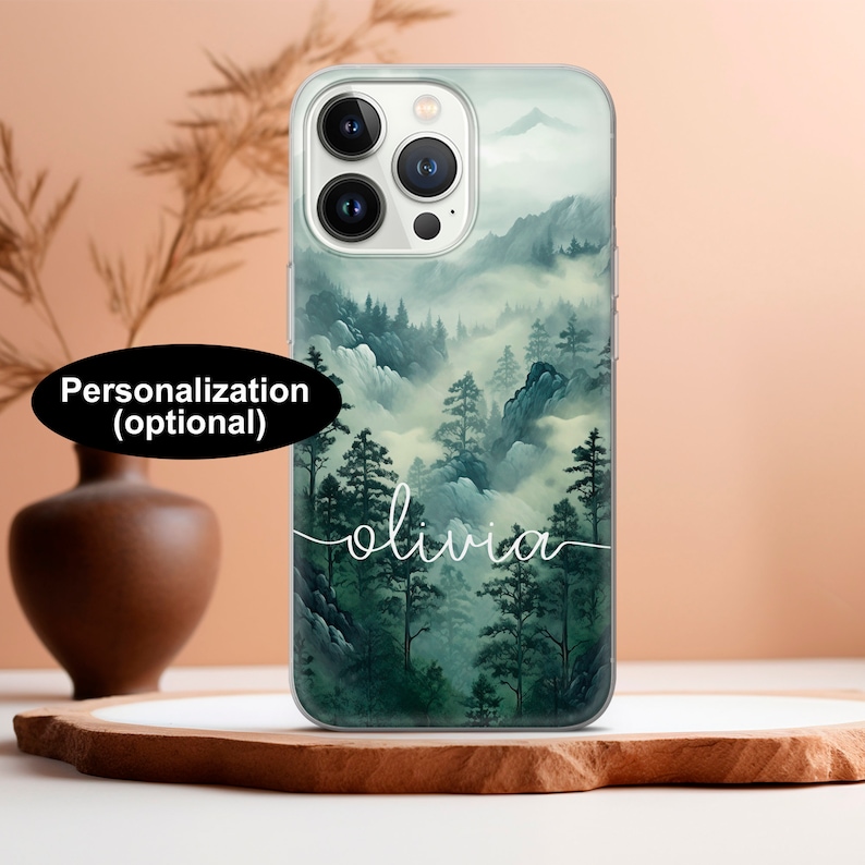 May include: Clear phone case featuring a misty mountain landscape with green and gray hues. The name "olivia" is written in white script across the bottom. The text "Personalization (optional)" is in a black oval.