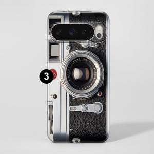Pu&ograve; includere: Custodia trasparente per telefono con un design di fotocamera vintage. La custodia ha una texture nera simile alla pelle sul lato destro, con dettagli argentati e neri. L'obiettivo della fotocamera &egrave; prominente.