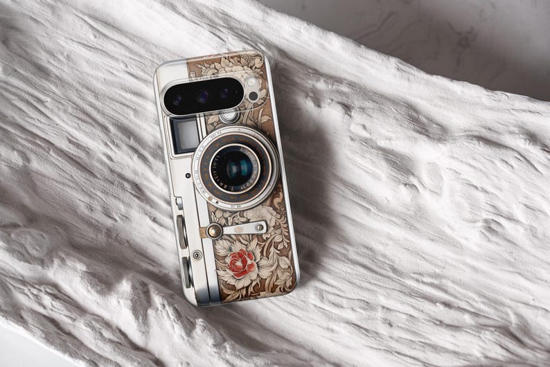 Pu&ograve; includere: Una custodia per telefono con un design di fotocamera vintage. La custodia presenta un motivo floreale dettagliato nei toni del marrone e del crema, con un accento di rosa rossa. L'obiettivo e i pulsanti della fotocamera sono rappresentati in modo realistico.