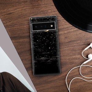 Puede incluir: Una funda de tel&eacute;fono negra con un dise&ntilde;o de noche estrellada. La funda presenta una luna creciente y nubes con detalles dorados.