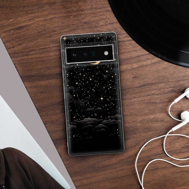 Puede incluir: Una funda de tel&eacute;fono negra con un dise&ntilde;o de noche estrellada. La funda presenta una luna creciente y nubes con detalles dorados.
