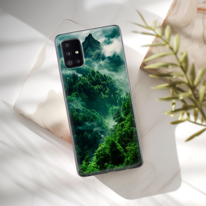 May include: A clear phone case with a green mountain and forest scene. The case has a raised camera bump with three lenses.