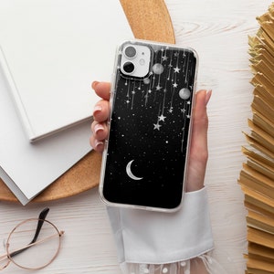 May include: A clear phone case with a black background and a white crescent moon, stars, and dangling ornaments.