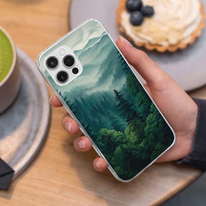 May include: Clear phone case featuring a landscape design of a forest with green trees and mountains. The case has a clear border and covers the back of the phone. The design has a watercolor effect.