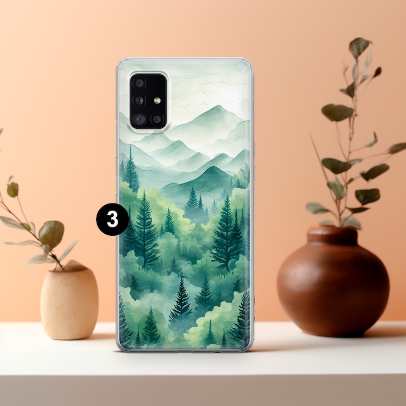 May include: A clear phone case featuring a watercolor landscape of green trees and mountains. The design has a soft, blurred effect, with varying shades of green and a light, airy feel. The number "3" is visible on the case.