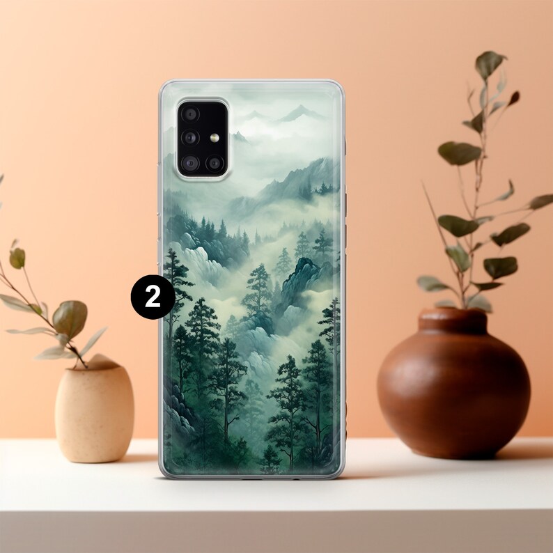 May include: A clear phone case featuring a landscape design of a misty mountain forest. The artwork showcases green trees, blue mountains, and white fog. The number "2" is printed in white on the case.