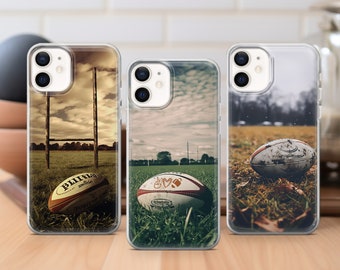 May include: Three clear phone cases with different rugby-themed designs. The first case features a rugby ball and goal posts on a grassy field. The second case features a rugby ball with a peace sign and heart design on a grassy field. The third case features a muddy rugby ball on a grassy field.