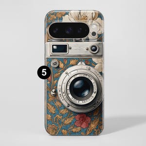 Pu&ograve; includere: Una custodia per telefono con un design a fotocamera vintage. La custodia ha uno sfondo blu con motivi floreali dorati, bianchi e rossi. L'obiettivo e i dettagli della fotocamera sono argentati.