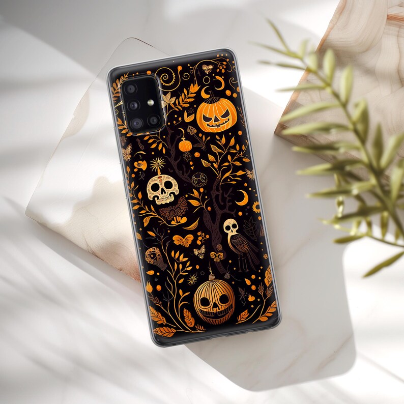 May include: A black phone case with a Halloween-themed design. The design features a black background with orange and yellow pumpkins, skulls, and owls. The design is surrounded by a gold-colored vine.