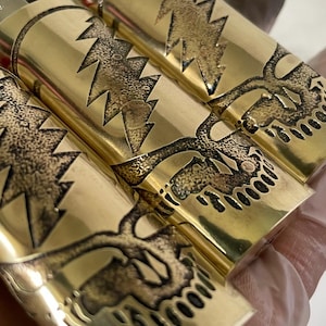 Peut inclure: Trois briquets en métal couleur or avec un crâne et un éclair gravés.