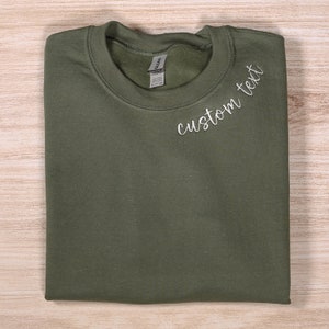 May include: A folded olive green sweatshirt with the text "custom text" embroidered on the front.