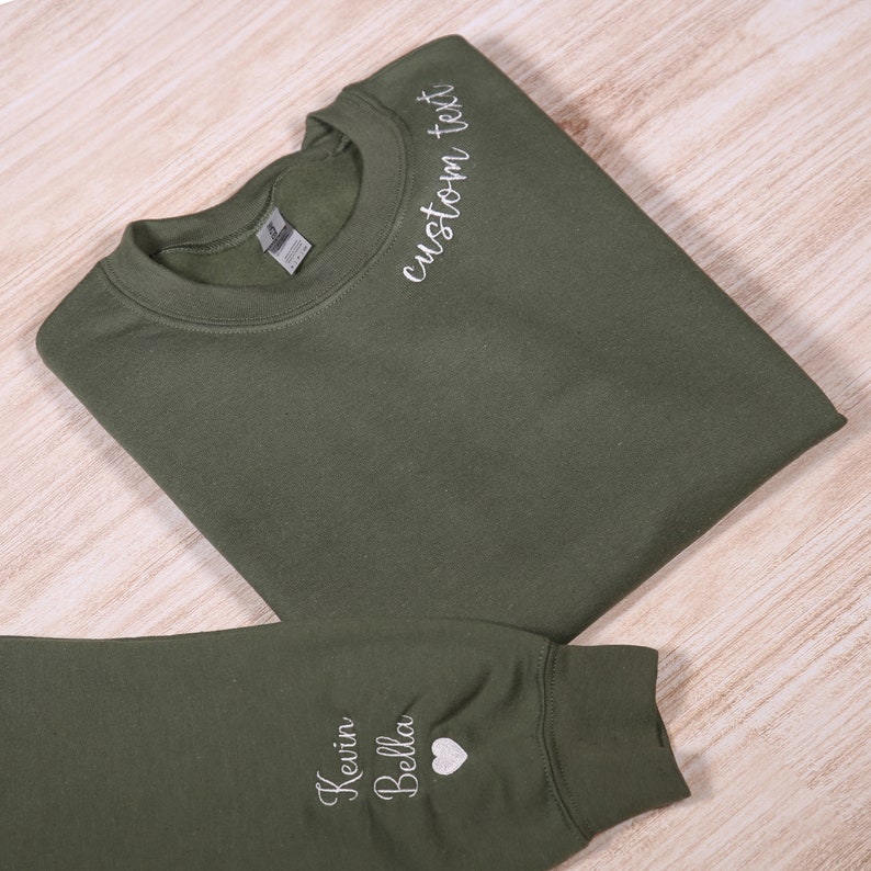 May include: A green sweatshirt with white embroidery. The front of the sweatshirt says "custom text" and the sleeve says "Kevin Bella" with a heart.