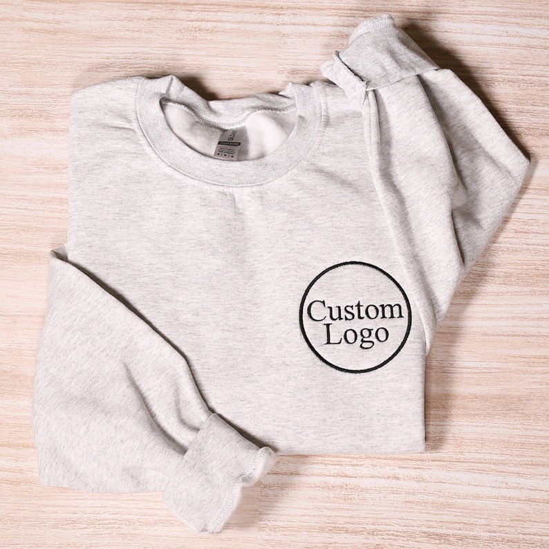 May include: A gray sweatshirt with a black circle and the text "Custom Logo" embroidered on the front.