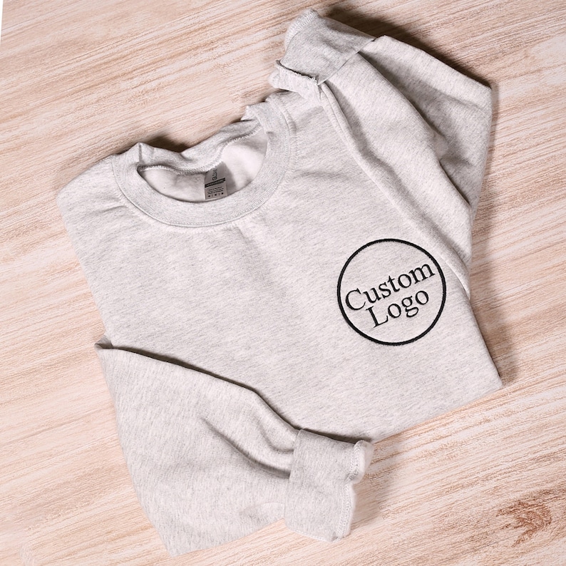May include: A gray sweatshirt with a black embroidered circle that says "Custom Logo" on it.