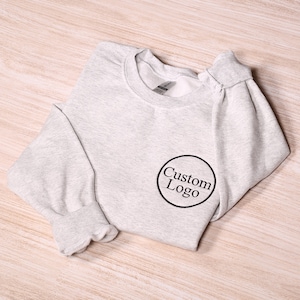 May include: A gray sweatshirt with a black circle and the text "Custom Logo" embroidered on the front.