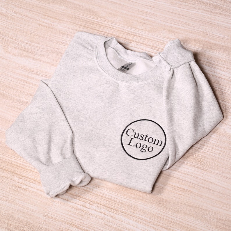May include: A gray sweatshirt with a black circle and the text "Custom Logo" embroidered on the front.