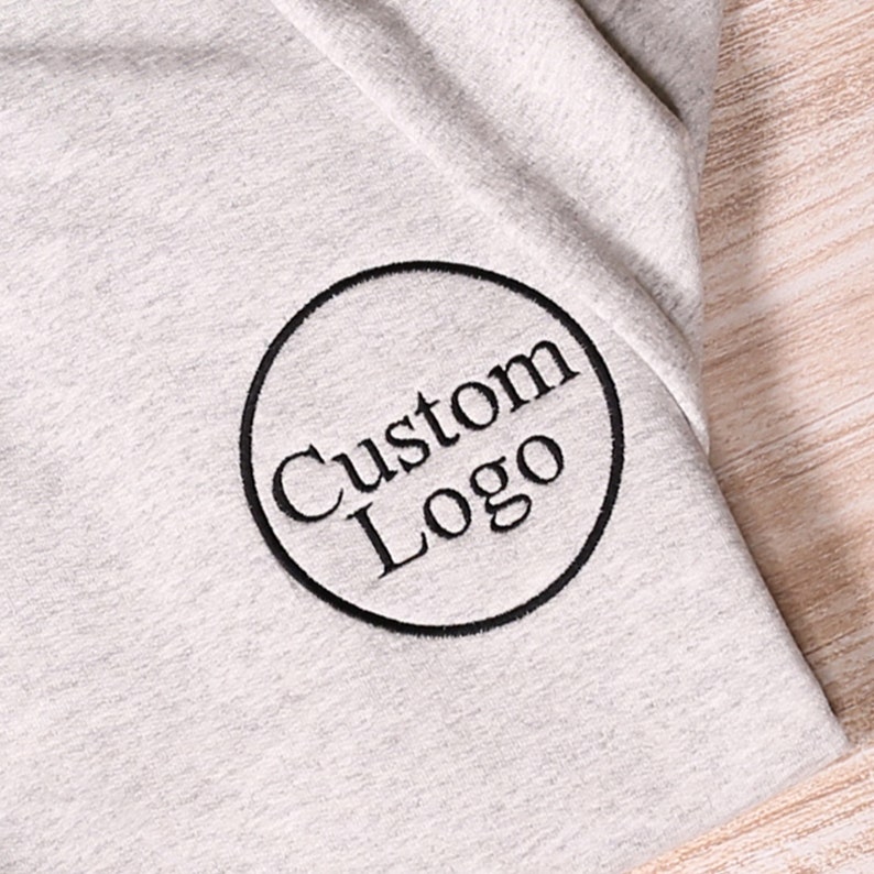 May include: A gray t-shirt with a black embroidered circle that says "Custom Logo" on it.